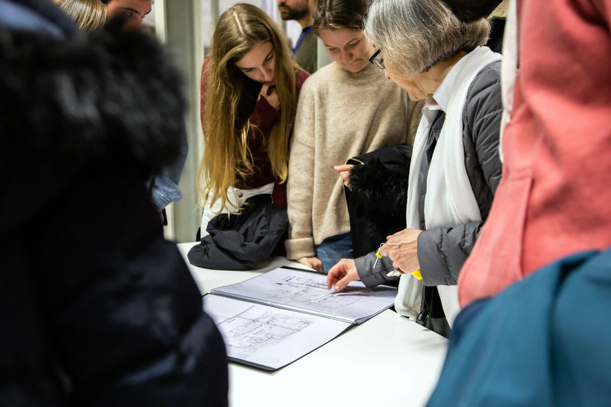 Participants engaging in group discussion over drawings during an architectural workshop with Ana Fernández