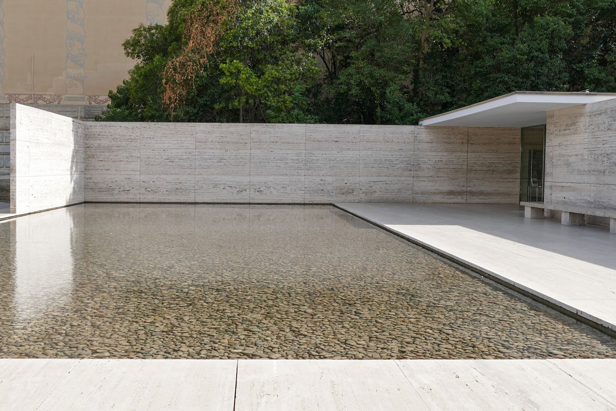 U-shaped travertine wall and travertine floor around front pool filled with pebbles in the Barcelona pavilion