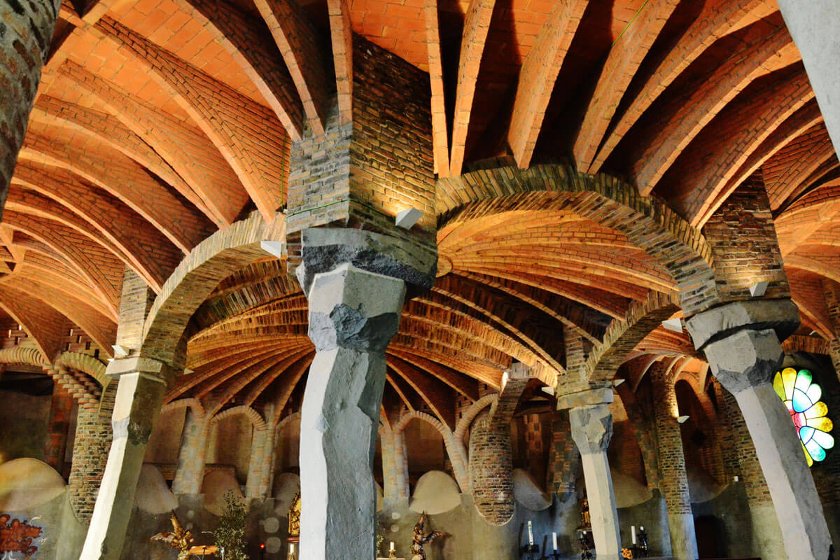 Güell Crypt interior with vaulted ceiling, columns of basaltic stone and brick pillars