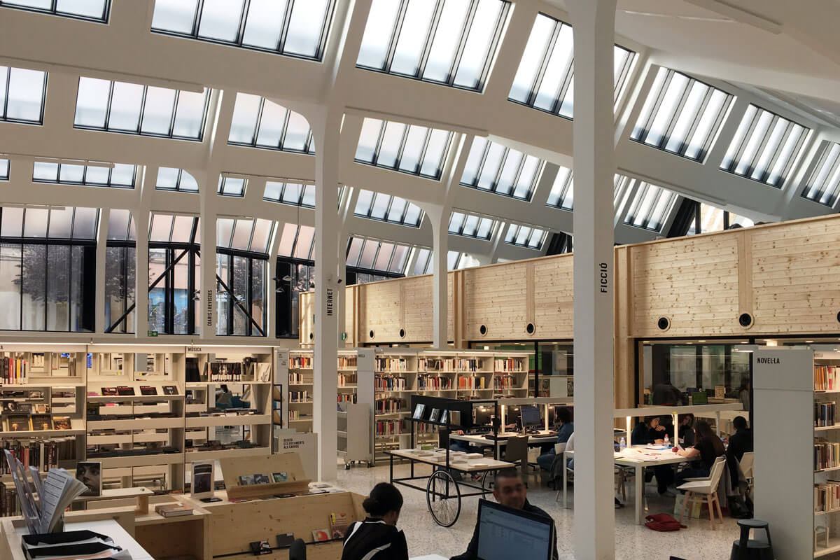 Luminous interior of a district library in preserved textile factory featuring a saw-tooth roof