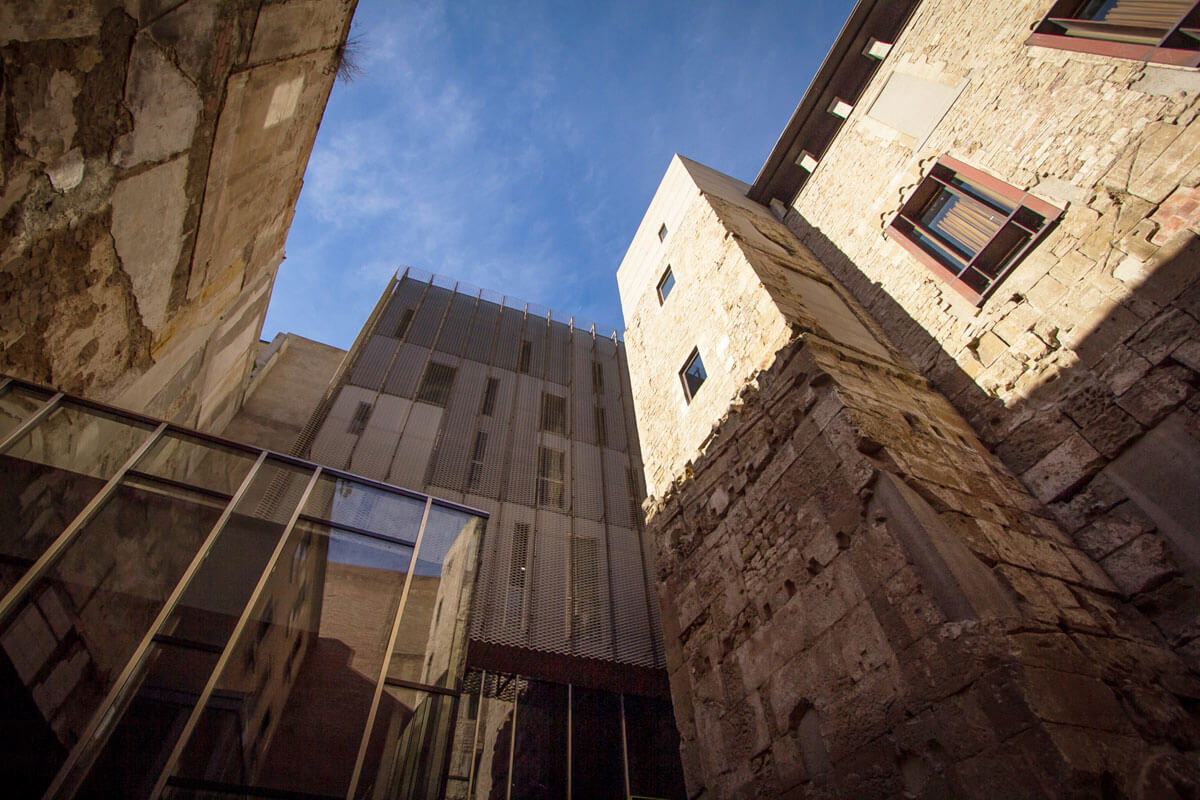 Building ensemble layered through the passage of time, with section of Roman wall and defense tower